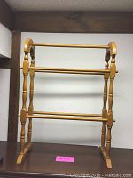 Full frontal view of the wooden quilt rack showing three horizontal bars and turned legs with arched top supports.