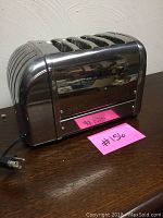 Side view of the polished stainless steel four slice Dualit toaster with power cord visible.