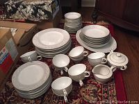 Full view of all china pieces arranged on floor including plates, cups, large platter, sugar bowl and creamer.