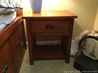 Front view of the wooden night stand positioned beside a bed, showing drawer and open shelf