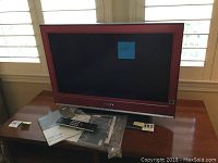 Front view of Sony Bravia TV on wooden table with remote and manuals.