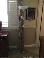 Full view of the metal floor lamp showing its height and placement near a window with curtains.