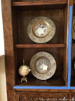 Display of two decorative plates and one stone globe décor in a wooden shelf unit.