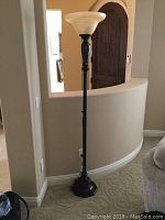 Full view of the floor lamp showing the black metal base, pole, and beige glass shade in a room.