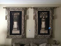 Two wall tapestries side by side hanging above a sofa, each showing different classical columns with ornate borders and mounted on rods with tassels.