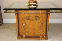 Front view of the leather trunk used as a base showing detailed metal hardware and straps.