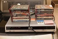 Front view of black Panasonic DMR-EH50 DVD player with two stacks of DVDs on top, some movie titles visible, power cable connected.