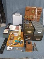 Wide view of vintage office items including wooden box, metal drawers, various office tools and organizers.