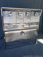 Front view of closed chrome pantry storage unit showing four labeled canister compartments for sugar, tea, coffee, flour and lower bread box.