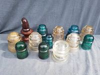 Full set of 14 glass insulators in varying colors and shapes displayed on grey fabric background.