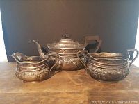 Three-piece tea service set comprising teapot, creamer, and sugar bowl showing overall design and condition on wooden surface