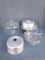 All items together: two glass cake plates with domes, stainless steel cake stand and two metal lids.