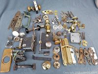 Full lot laid out on a grey cloth showing a variety of door knobs, keyhole plates, lock parts, and other hardware pieces with diverse finishes like brass, black, and white ceramic.