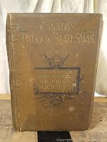 Front cover of the brown hardcover book titled 'Canada's Patriot Statesman' with gold embossed lettering and decorative design.