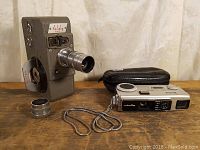 Photo showing the full view of the Holiday 8mm wind-up movie camera, detachable lens piece on the table, and the Minolta 110 spy camera with its case.