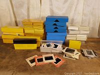 Full view of collection showing yellow, blue, and white storage boxes with stacks of mounted 35mm slides spread out in front.