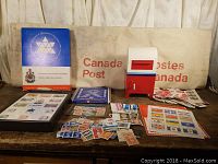 Photo showing 1986 Canada Post canvas mail bag, replica mailbox, blue stamp box, stamp booklets, loose stamps, and commemorative stamp box.