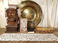 Photo of the full collection including wooden Christ carving, brass praying hands sculpture, brass tray, mother-of-pearl psalm book, and decorative box laid on lace cloth