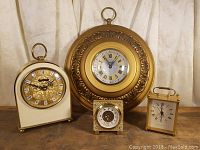 Photo of four clocks grouped together on a flat surface featuring various styles and sizes with clock faces visible.
