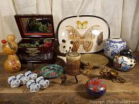 Full view of assorted Asian decorative items: cloisonné box, ginger jar, moth display, figurines, small boxes and plates.