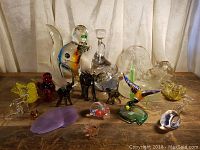 Wide view of collection of 21 colorful glass animal figurines on wooden surface with white curtain backdrop