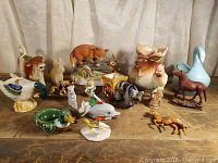 Assorted ceramic animal figurines including creamers, birds, horses, and other animals arranged on a wooden surface