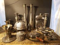 Full view of entire collection showing multiple silver plate candle holders, a domed serving cover, tray with knife, carousel coin bank and other items on wood surface.