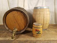 Three wooden barrels shown, two larger oak barrels including one with brass tap, and one small decorated coin bank barrel with floral design and 'Mittenwald' label.