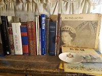 Shows the full collection of books and Globe and Mail newspaper with Queen Elizabeth II on cover along with fold-out map and decorative plate.