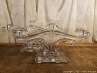 Pair of clear glass candle holders with elegant curved arms and five candle cups each on a wooden table.