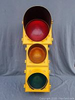 Front view of the traffic light showing red, yellow, and green lenses stacked vertically, housed in yellow acrylic with visors.