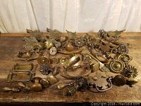 Overall view showing multiple brass drawer pulls, knobs, escutcheons, and handles arranged on wooden surface.