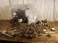 Photo showing a variety of drawer pulls including large ornate metal pulls, white ceramic pulls in bags, and smaller metal handles on a wooden surface.