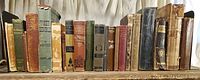 Photo showing a variety of antique books lined up on a shelf with visible aging and wear.