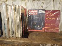 Side view showing multiple vintage books and magazines on radio and television in protective sleeves on wooden shelf.