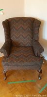 Front view of wingback chair showing patterned fabric upholstery, rolled arms, and cabriole legs.