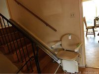 Side view of the beige chair lift mounted on the staircase rail, showing seat and rail length.