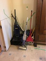 Photo of upright blue Kenmore vacuum cleaner, small stool, broom, and dustpan with other household items