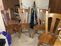 Four solid wooden chairs arranged in a room showing front and slight side views.