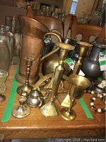 Photo of various brass candle sticks, copper jug, brass vase and other decorative metal items including silver plated bell and pewter certificate holder arranged on table