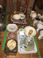 Wide view of assorted serving items including bowls, glass canisters, mortar and pestle, candlesticks, and mugs on a table.
