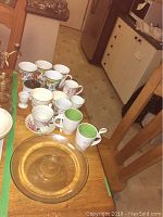 View of all mugs, spoons, and glass cake dish on a wooden surface, showing variety and condition including minor chips on mugs