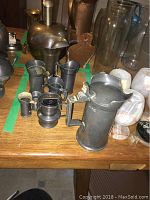 Photo showing the full set with the largest pewter measuring cup with handle in front and smaller units behind on wooden table.