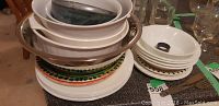 Stack of plates, bowls, and large mixing bowl arranged on a table; includes white plates and bowls along with patterned plates and a metal mixing bowl.