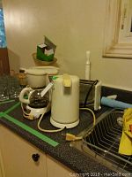 Sunbeam 4-cup coffee maker, Sunbeam cordless kettle, with additional appliances and kitchen items on kitchen counter near sink.