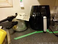 Philips Rapid Air Cooker and Jasi pressure cooker with manual on kitchen counter.