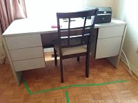 Full view of grey desk with five drawers and wooden chair placed in front, black briefcase and JVC speaker on desk surface