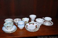 All nine teacups and matching saucers arranged side by side showing the diverse patterns and colors.
