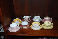Full view of all eight teacups and saucers arranged on wooden shelf, showcasing different floral patterns and colors