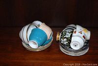 Two stacks of assorted teacups and saucers including colorful pastel shades and floral patterns